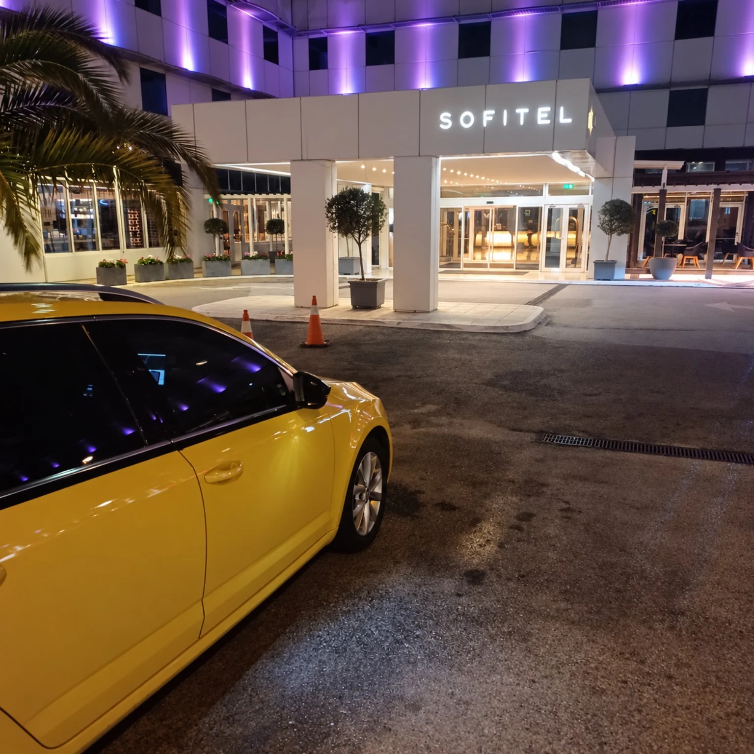 Yellow taxi outside the illuminated Sofitel Athens entrance